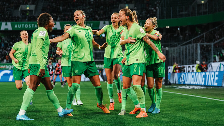 Die Spielerinnen des VfL Wolfsburg stehen auf dem Fußballplatz in der Volkswagen Arena und jubeln miteinander.