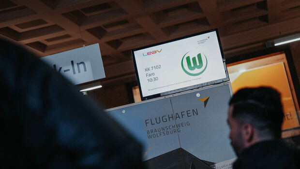 Das Logo vom VfL-Wolfsburg auf einem Bildschirm am Flughafen.