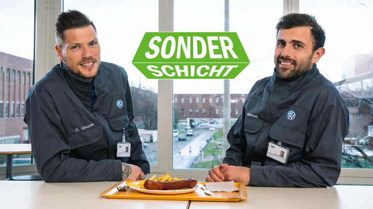 Daniel Gizcek und Admir Mehmedi lächelnd im VW-Overall während ihrer Schicht - dacor eine Volkswagen Currywurst. 
