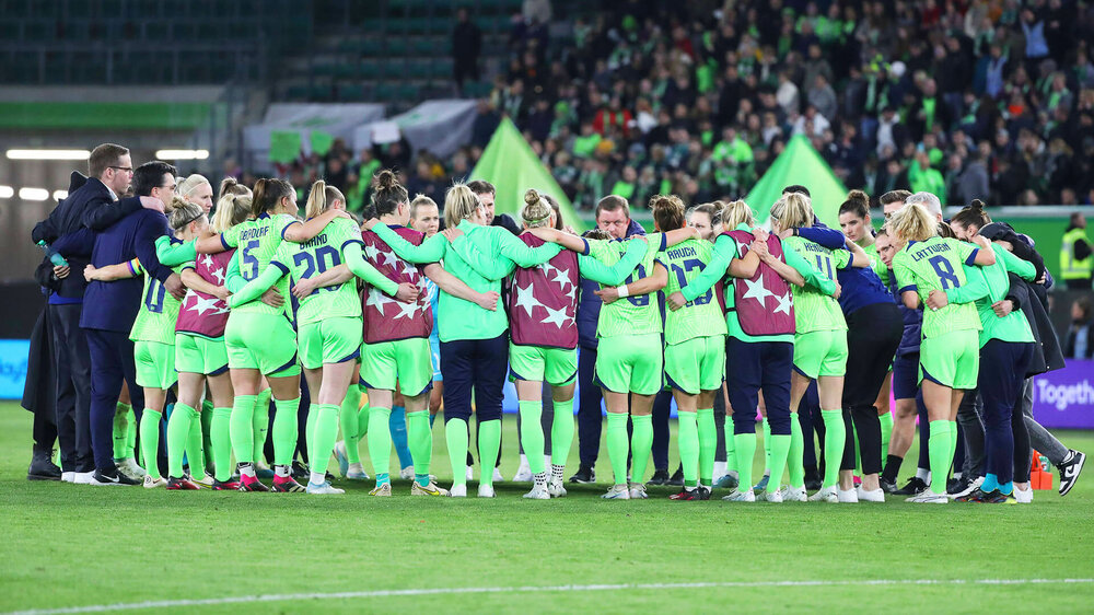 Die Spielerinnen des VfL-Wolfsburg liegen sich in den Armen und feiern einen Sieg mit den Fans.