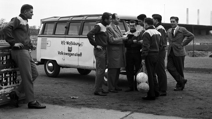 Einige Menschen versammeln sich vor einem VW-Bus. 