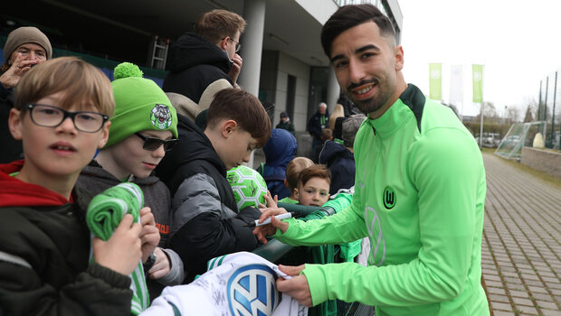 Mohammed Amoura signiert Fanartikel für kleine Fans und lächelt in die Kamera.