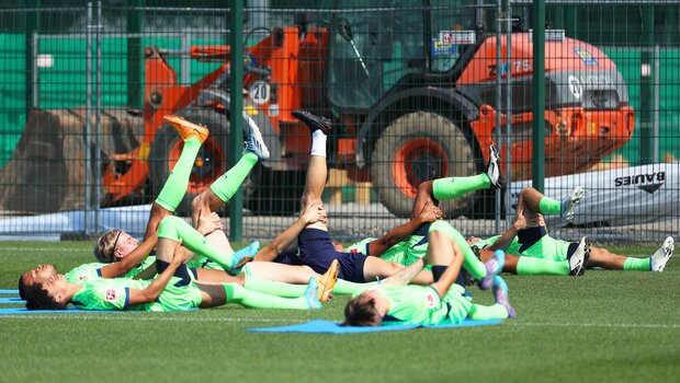 Die Männer des VfL Wolfsburg liegen in ihren neuen Trikots auf Trainingsmatten und dehnen die Beine.