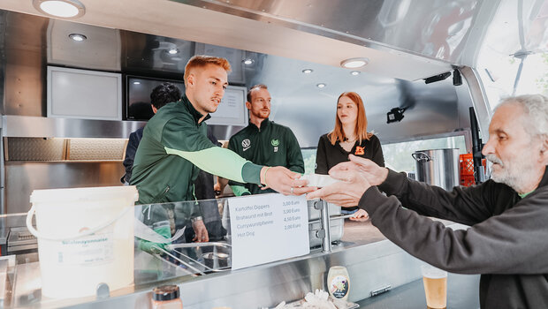 Maximilian Arnold und Kilian Fischer vom VfL Wolfsburg stehen im Getränkewagen. Fischer gibt grad ein Bier an einen Mann raus.