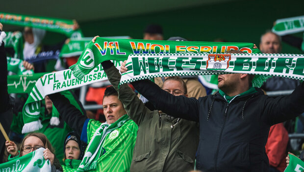 VfL Wolfsburg Fans halten im Stadion Schals in die Höhe.