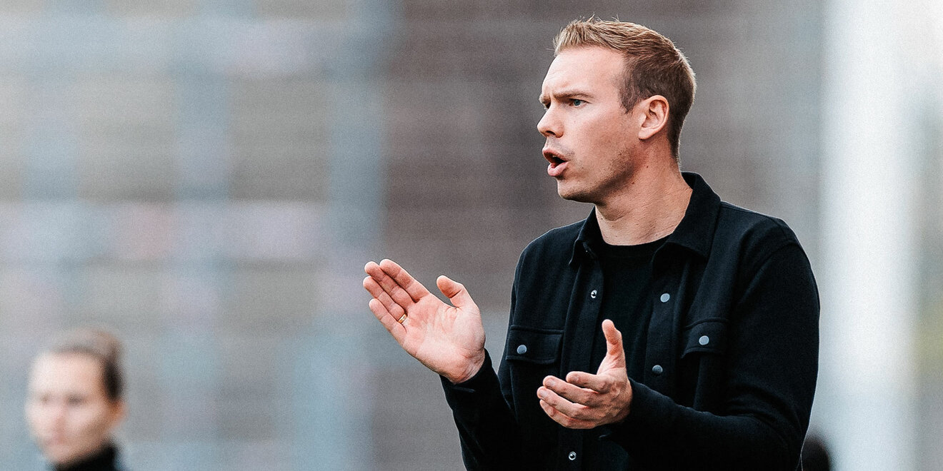 VfL Wolfsburg Trainer Tommy Stroot klatscht in die Hände und ruft vom Seitenrand etwas in Richtung Spielfeld.