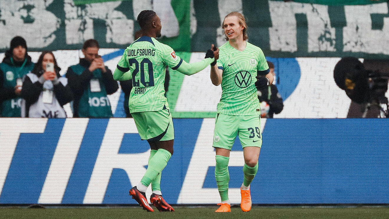 Die VfL Wolfsburg Spieler Wimmer und Baku klatschen sich auf dem Spielfeld ab.