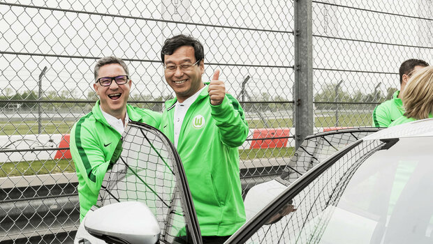 Zwei Partner des VfL Wolfsburg stehen am Auto und lachen in die Kamera.