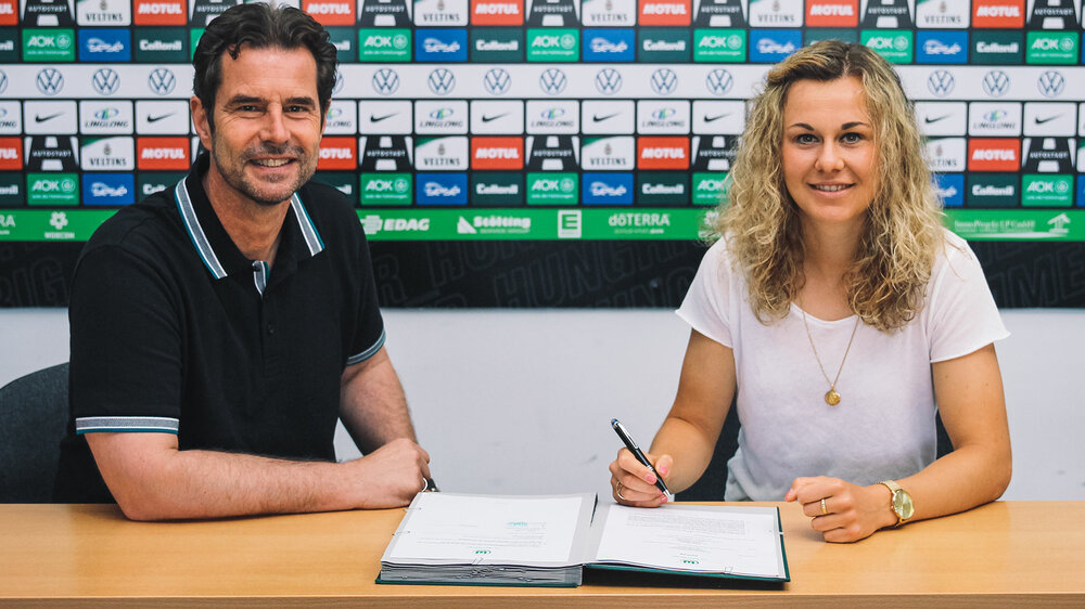 Ralf Kellerman und VfL-Wolfsburg-Spielerin Lena Lattweil sitzen an einem Tisch und Lena unterschreibt einen neuen Vertrag.