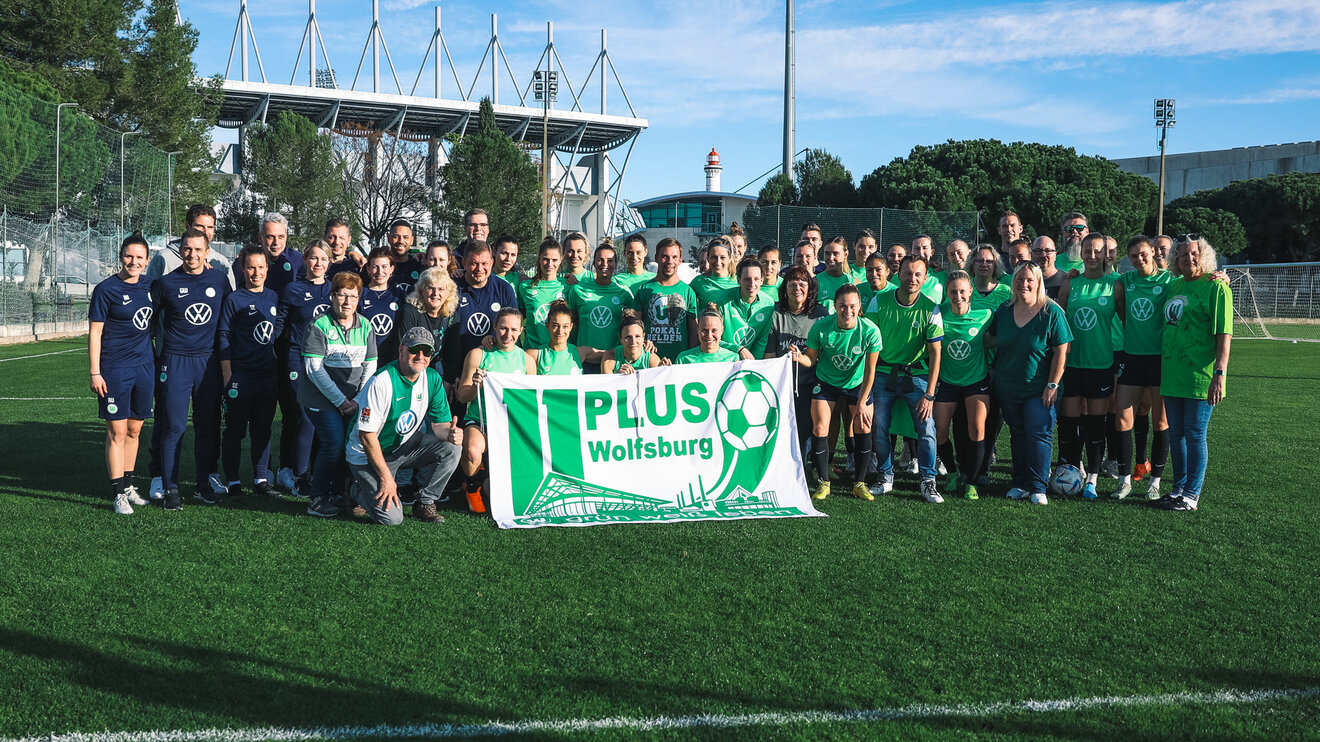Fans des VfL Wolfsburg posieren mit den Wölfinnen für ein Gruppenbild.
