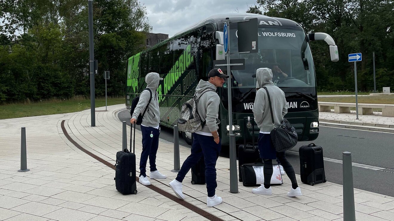 Drei Spieler des VfL Wolfsburg mit Koffern vor dem Mannschaftsbus.
