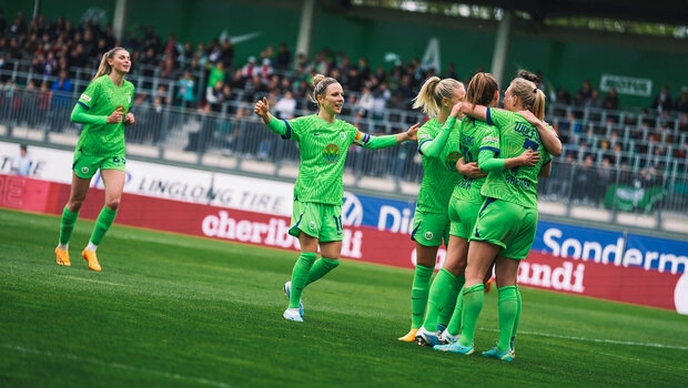 VfL Wolfsburg Spielerinnen umarmen sich und jubeln auf dem Spielfeld.