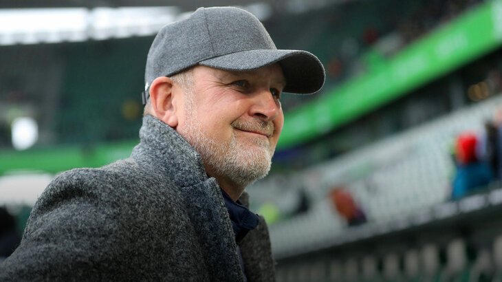 VfL Wolfsburg Geschäftsführer Schmadtke grinst bei einem Spiel in die Kamera.
