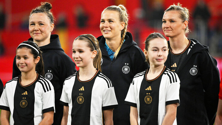 Marina Hegering, Merle Frohms und Alexander Popp vom VfL Wolfsburg stehen im Dress der Nationalmannschaft hinter Einlaufkindern.
