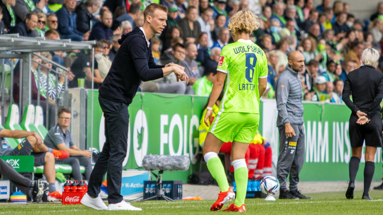 VfL Wolfsburg-Trainer Stroot gibt einer Spielerin vom Spielfeldrand aus Anweisungen.