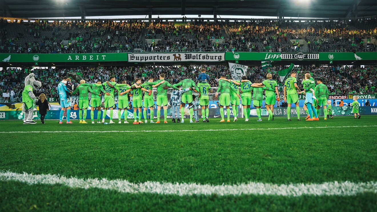 Die Mannschaft des VfL-Wolfsburg steht gemeinsam vor der heimischen Kurve der Fans in der Volkswagen Arena und zelebrieren gemeinsam.