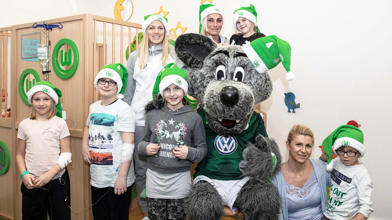 Lara Dickenmann, Jana Burmeister und Wölfi lachnend mit Kindern während des Krankenhausbesuchs.