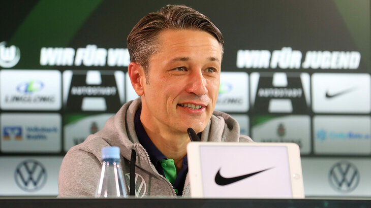 Der VfL Wolfsburg-Trainer lächelt bei der Pressekonferenz.