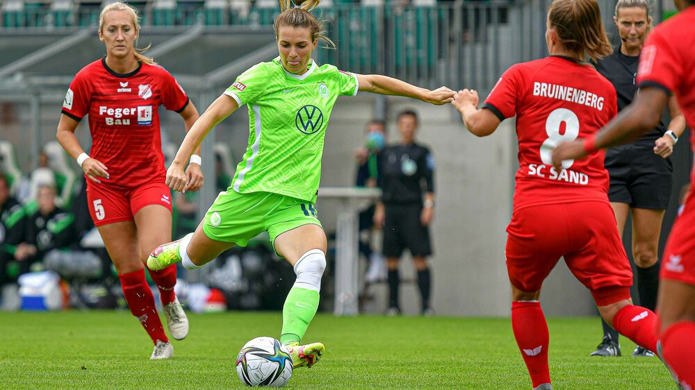Smits holt, um ringt von zwei Gegnerinnen, beherzt zum Tritt gegen den Ball aus im Spiel des VfL Wolfsburg gegen FC Sand.