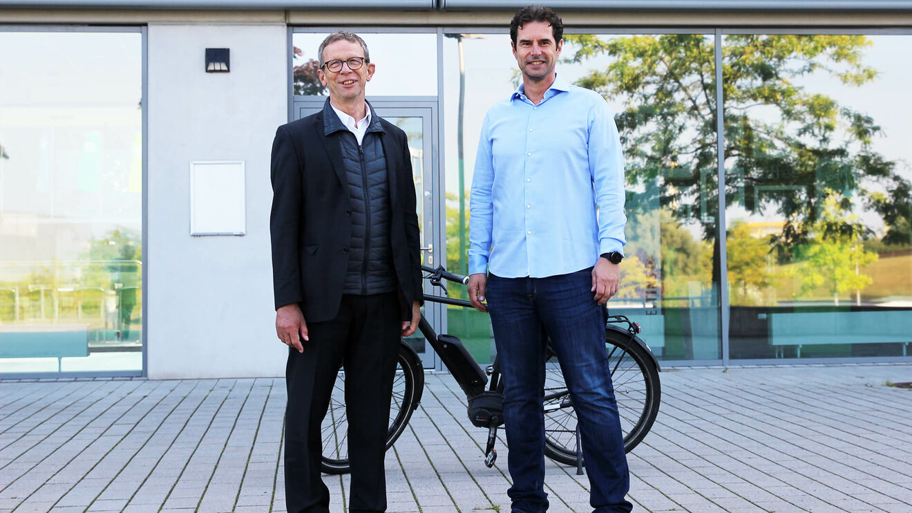 Zwei Personen aus dem Aufsichtsrat des VfL-Wolfsburg, Kellermann und Mohrs, posieren vor einem E-Bike.