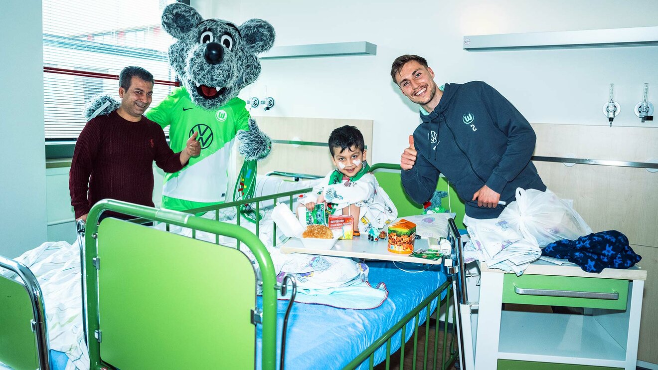 Kilian Fischer während eines Besuchs in der Kinderklinik Wolfsburg zusammen mit einem Kind, dessen Vater und Wölfi. 