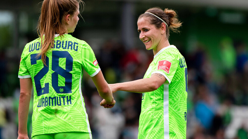Waßmuth und Blässe vom VfL Wolfsburg klatschen sich lächelnd auf dem Spielfeld ab.