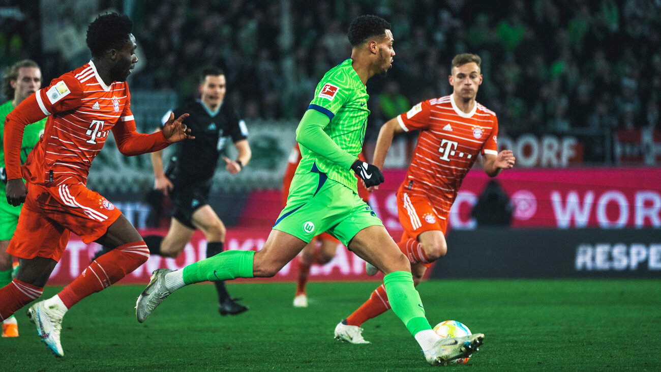 VfL-Wolfsburg-Spieler Lukas Nmecha ist von den Gegenspielern aus Bayern umgeben und läuft vorwärts.