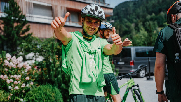VfL-Wolfsburg-Spieler Kilian Fischer trägt einen Fahrradhelm und reckt zwei Daumen in die Luft.