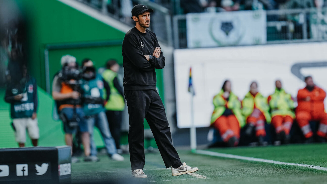 Der Freiburg-Trainer Julian Schuster steht an der Seitenlinie mit verschränkten Armen.