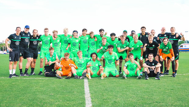 Die Spieler und Trainer aus der VfL Wolfsburg-Akademie stellen sich für ein Gruppenfoto auf dem Platz auf.
