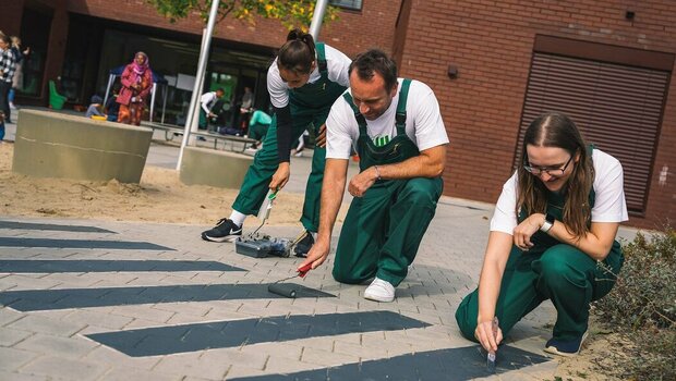 VfL Wolfsburg Mitarbeiter malen einen Zebrastreifen auf den Boden im Kindergarten am "Wir-für euch"-Tag.