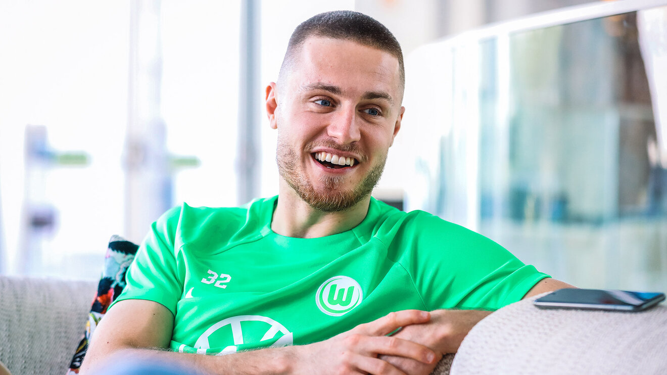 VfL-Wolfsburg-Spieler Mattias Svanberg sitzt auf einem Sofa, gibt ein Interview und lacht.