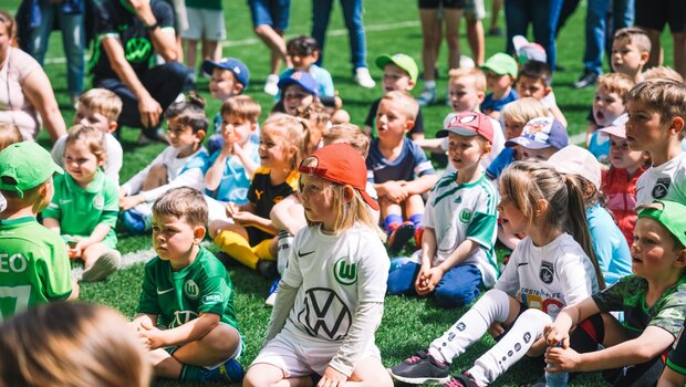 Die WölfiClub Mitglieder sitzen gespannt auf dem Spielfeld des VfL Wolfsburg.