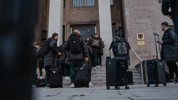 Die VfL-Wolfsburg-Spieler stehen mit ihren Koffern vor dem Flughafen.