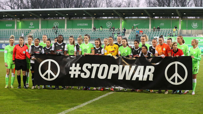 Die Mannschaften der VfL Wolfsburg Frauen und des FC Sand posieren vor ihrem Spiel gemeinsam mit einem STOP WAR Banner im AOK Stadion.