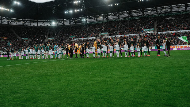 Die Mannschaften vom VfL Wolfsburg und Augsburg stehen nebeneinander auf dem Platz und winken den Fans.