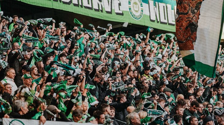 Fans des VfL Wolfsburg schwenken auf der Tribüne grün-weiße Schals.