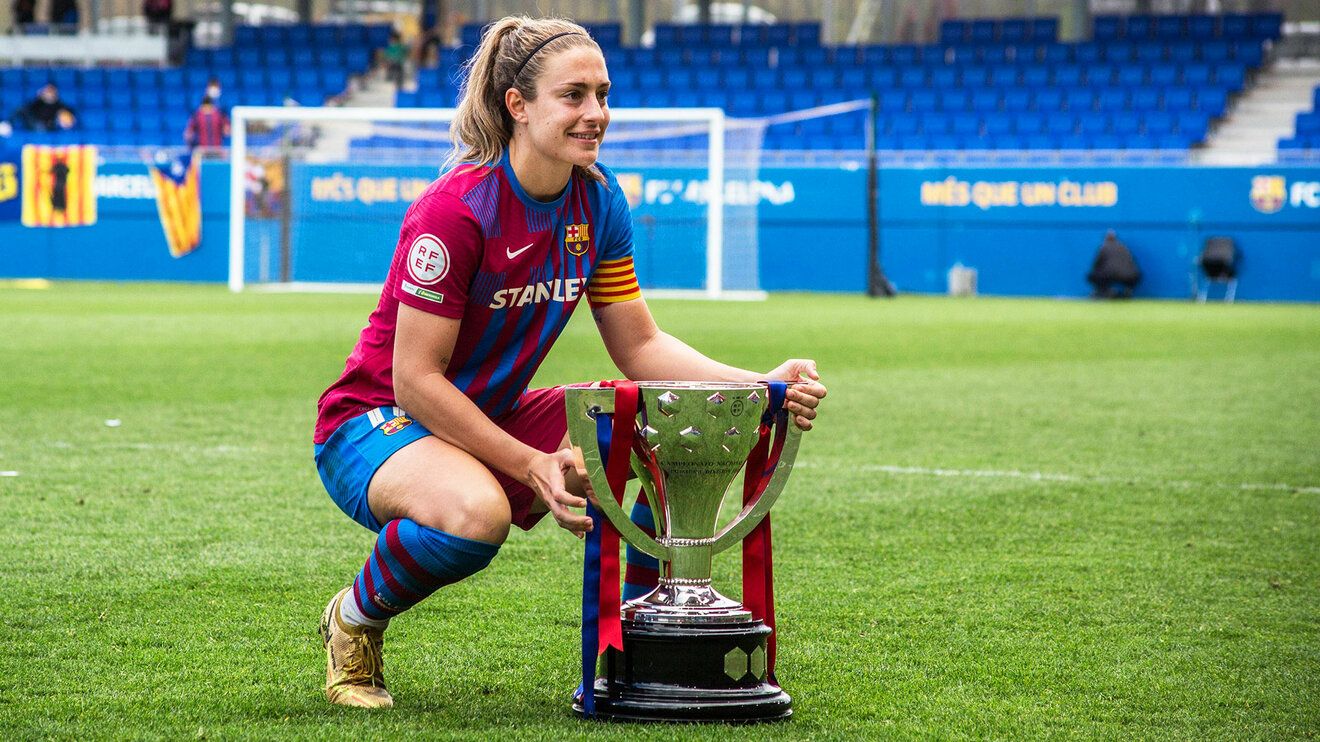 Alexia Putellas vom FC Barcelona Femeni kniet auf dem Platz neben dem UWCL Pokal.