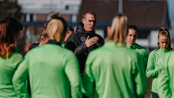 VfL-Wolfsburg-Trainer Tommy Stroot steht inmitten seiner Spielerinnne und hält eine Ansprache.