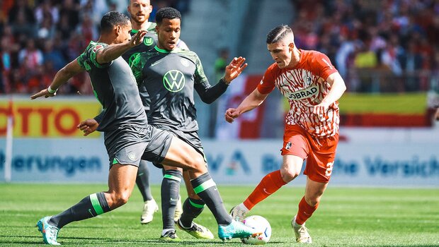 Die beiden VfL Wolfsburg-Spieler Maxence Lacroix und Aster Vranckx im Kampf um den Ball mit einem Gegenspieler.