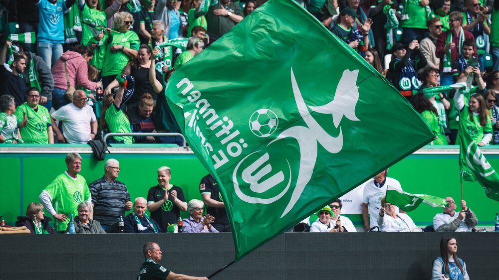 Ein Fan der Frauenmannschaft des VfL Wolfsburg schwenkt eine Fahne vor der Tribüne.