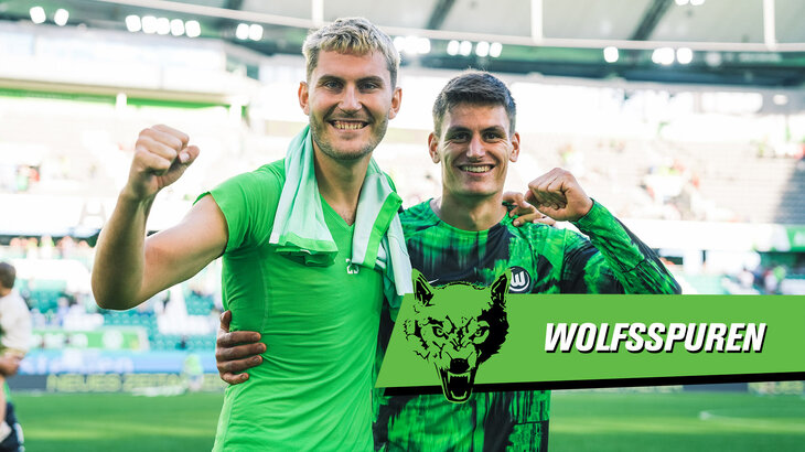 Die beiden VfL-Wolfsburg-Spieler Jonas Wind und Joakim Maehle stehen Arm in Arm, ballen jeweils eine Faust und lachen indie Kamera.