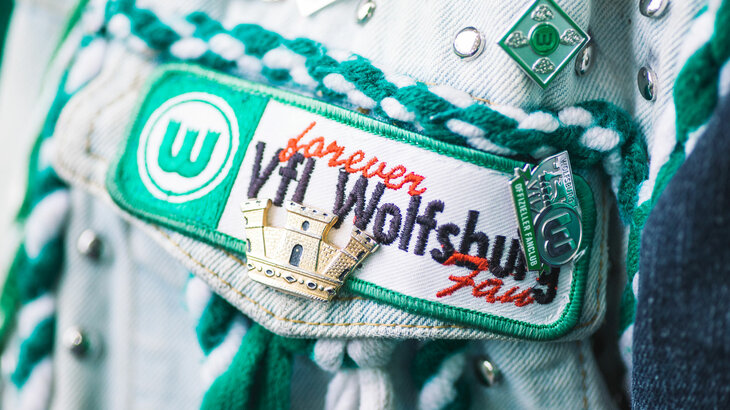 Das VfL-Logo und eine Stecknadel auf der Jeansjacke eines VfL Wolfsburg Fans.