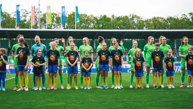 Die VfL Wolfsburg Spielerinnen stehen vor dem Spiel mit den Einlaufkindern auf dem Platz.