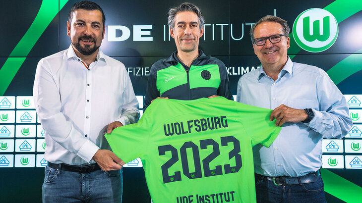 Der neue Geschäftspartner des VfL-Wolfsburg hält ein Trikot als Zeichen der Zusammenarbeit hoch.