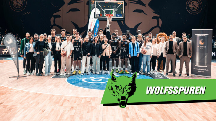 Eine VfL-Wolfsburg-Grafik mit der Aufschrift "Wolfsspuren" liegt auf einem Gruppenfoto der Basketball Löwen aus Braunschweig und den Frauen des VfL.