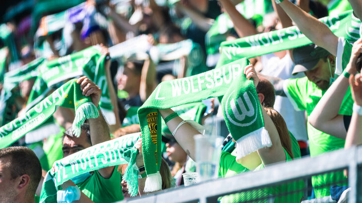 VfL Wolfsburg Fans halten in der Nordkurve Fanschals in die Höhe.