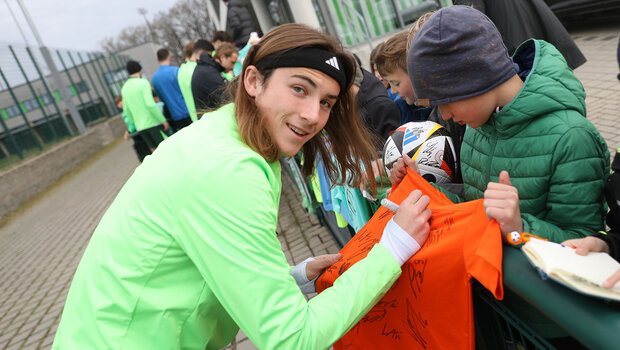 Bennit Bröger signiert Fanartikel für kleine Fans und lächelt in die Kamera.