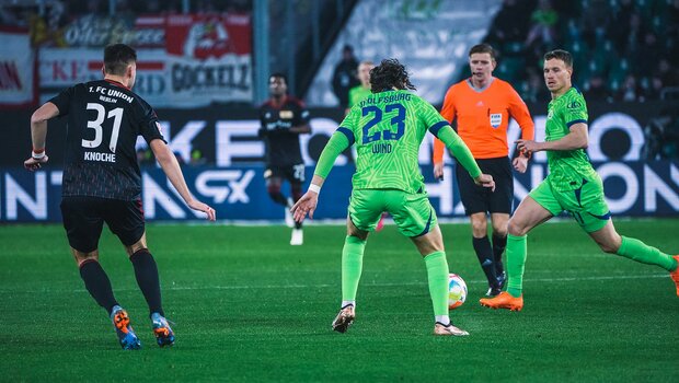 VfL-Wolfsburg-Spieler Yannick Gerhardt läuft zum Ball. Jonas Wind steht mit dem Rücken zur Kamera und schaut ihm zu.