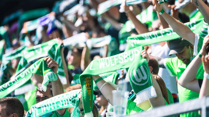 VfL Wolfsburg Fans in der Nordkurve halten ihre Schals in die Höhe.